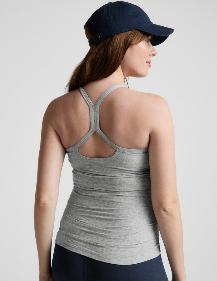 Woman wearing a gray maternity tank top and navy cap on a light gray background.