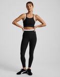 Woman wearing a black sports bra and leggings on a light gray background.