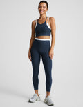 Woman wearing a navy sports bra and leggings set on a plain background.