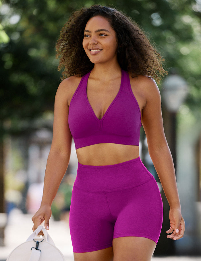 A woman wearing a matching magenta-purple activewear set consisting of a halter-neck sports bra and high-waisted biker shorts, walking outdoors on a blurred street background.