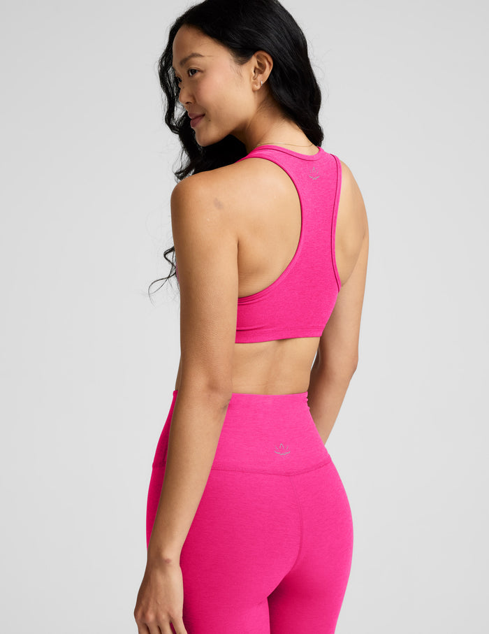 Woman wearing a pink sports bra and leggings on a gray background.
