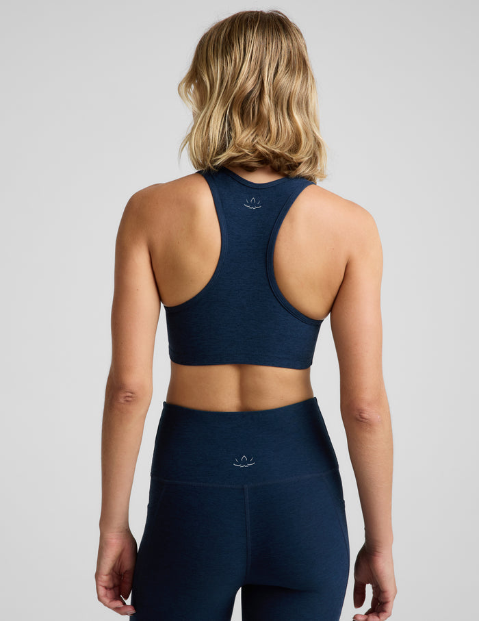 A woman shown from the back wearing a dark navy blue athletic sports bra and matching high-waisted leggings against a light gray studio background.