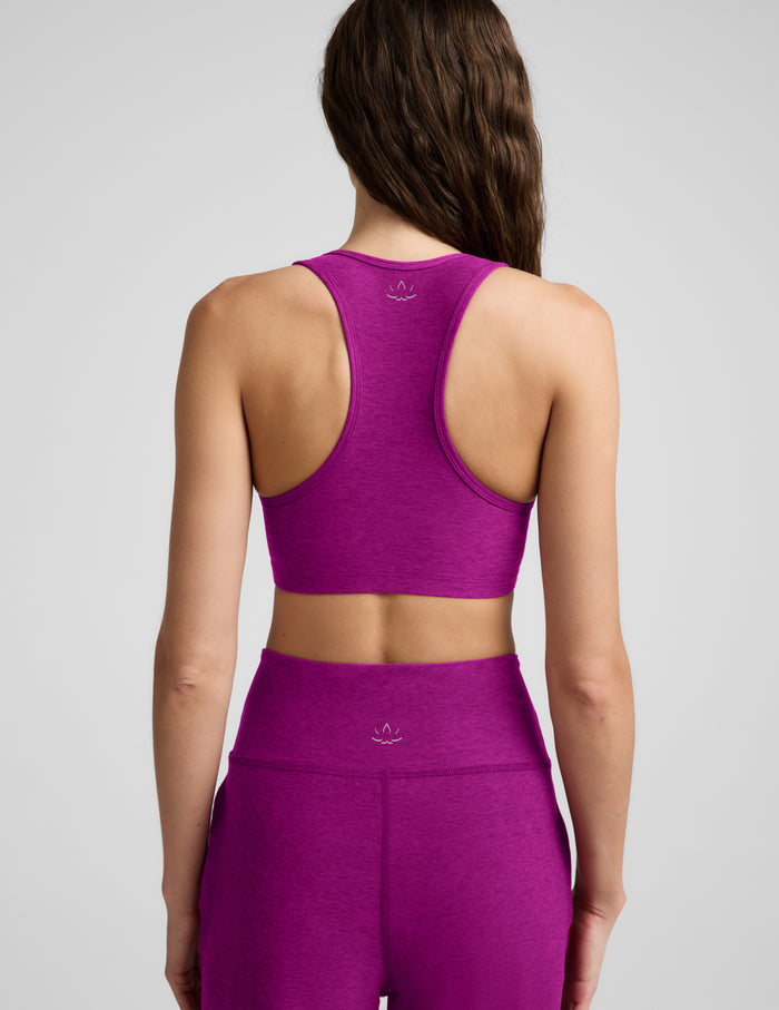 Woman wearing a purple bra and wide leg pants against a plain background.