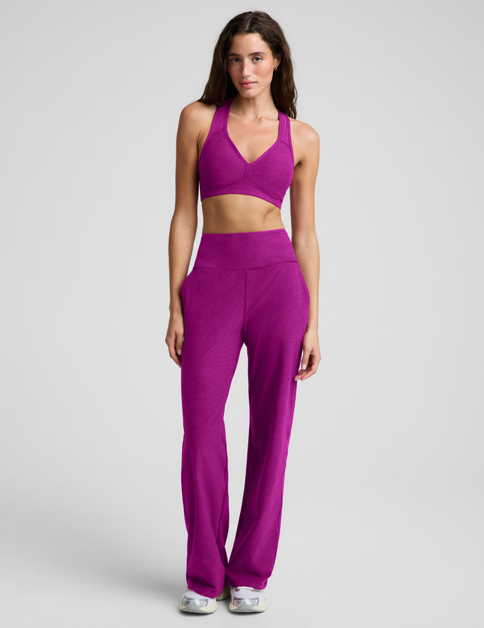 Woman wearing a purple bra and wide leg pants against a plain background.