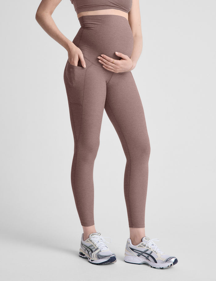 Woman wearing brown maternity leggings with pockets on a light gray background.