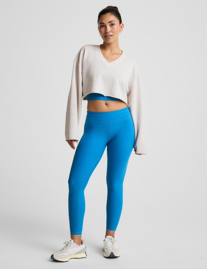 Woman wearing a white sweater and blue mid-rise leggings against a plain background.