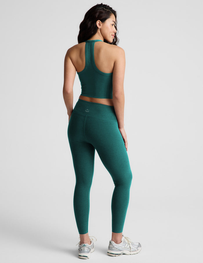 Woman wearing a green cropped tank and green mid-rise leggings against a plain background.