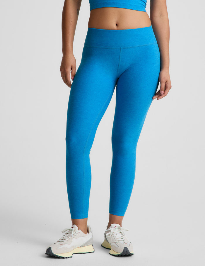 Woman wearing blue mid-rise leggings against a plain background.