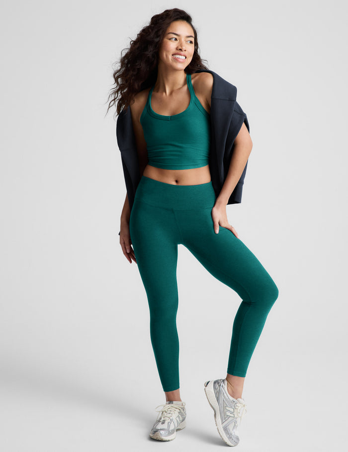 Woman wearing a green cropped tank and green mid-rise leggings against a plain background.
