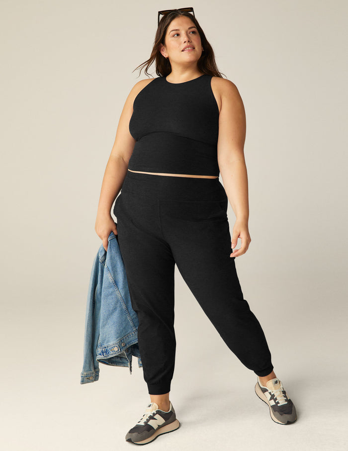 Woman wearing black Spacedye Midi Joggers with a wide waistband and tapered, banded cuffs, holding a denim jacket.