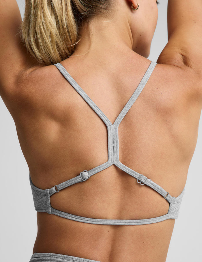A woman modeling a light heather gray sports bra and matching high-waisted leggings with a drawstring waist, photographed against a solid light gray studio background.