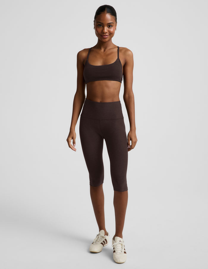 Woman wearing a brown bra and brown leggings against a plain background.