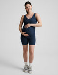 Pregnant woman wearing a navy blue maternity outfit on a light gray background.
