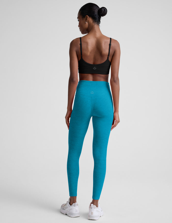 Woman wearing a black sports bra and blue leggings on a white background.