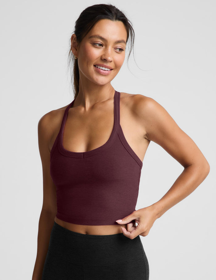 A woman modeling a scoop-neck athletic tank top in deep burgundy, paired with black athletic pants, against a solid light gray background.