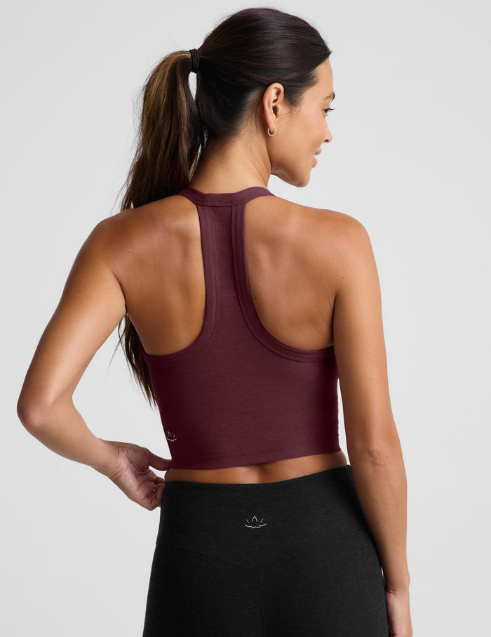 A woman modeling a scoop-neck athletic tank top in deep burgundy, paired with black athletic pants, against a solid light gray background.