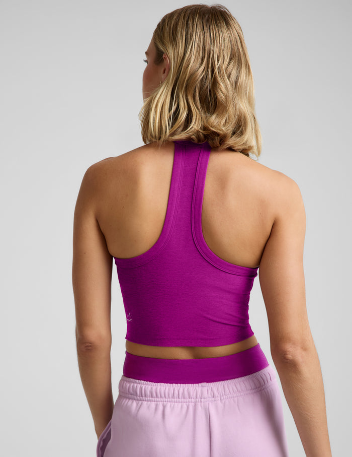 Woman wearing a purple cropped racerback tank top and purple sweatpants against a plain background.