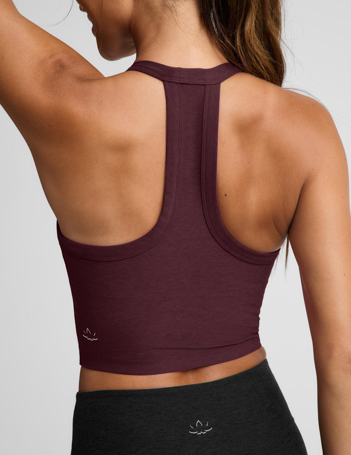 A woman modeling a scoop-neck athletic tank top in deep burgundy, paired with black athletic pants, against a solid light gray background.