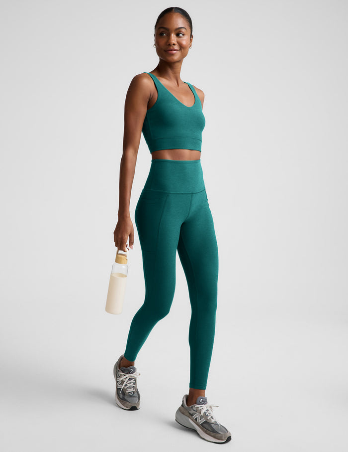 Woman wearing a green cropped tank and green leggings with pockets against a plain background.