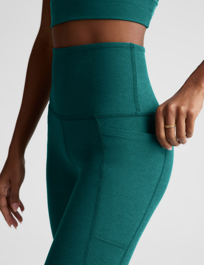 Woman wearing a green cropped tank and green leggings with pockets against a plain background.