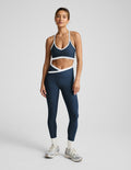 Woman wearing a navy sports bra and leggings set on a light gray background.