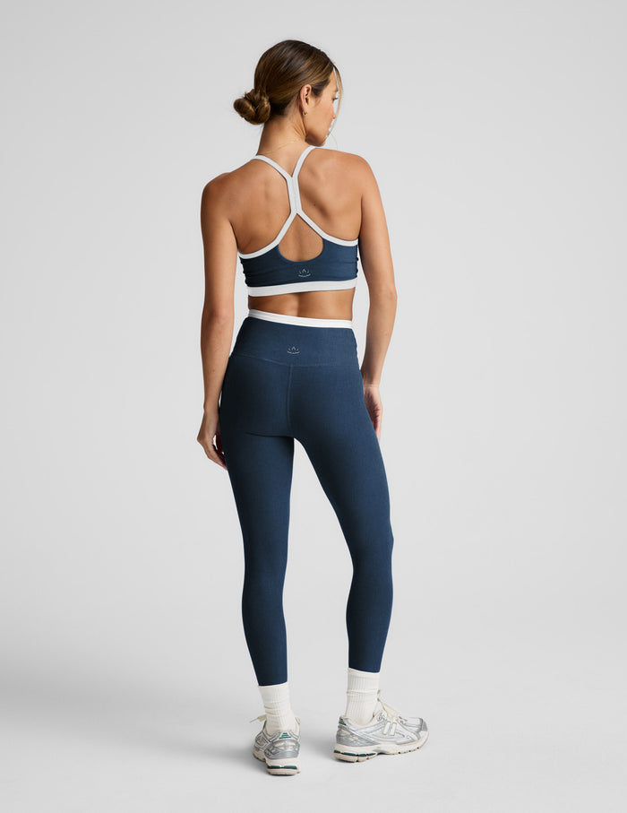 Woman wearing a navy sports bra and leggings set on a light gray background.