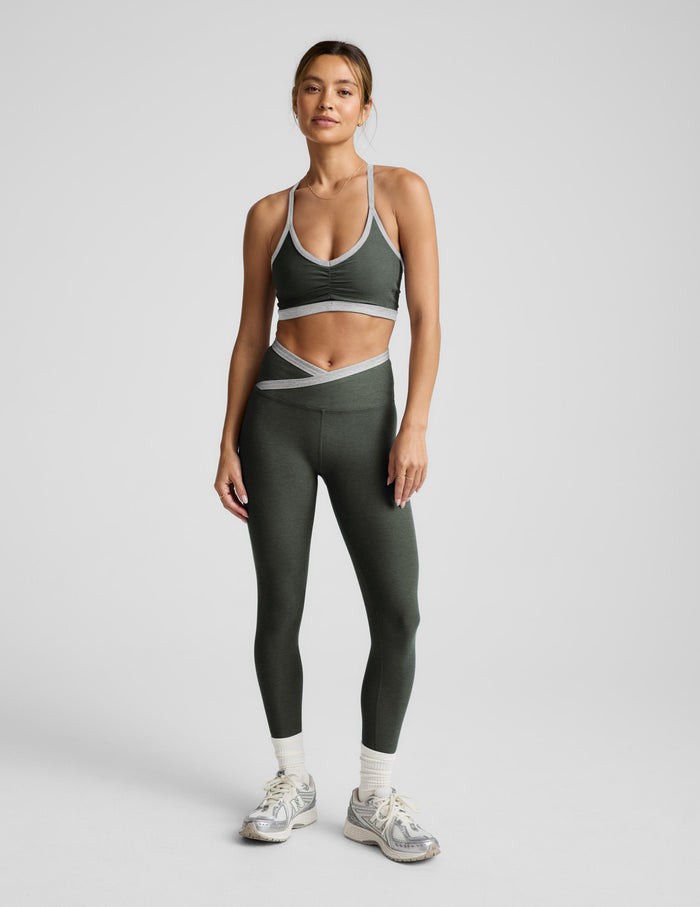Woman wearing a green athletic outfit with a sports bra and leggings on a light gray background.