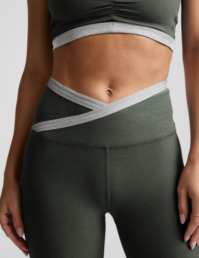 Person wearing dark green athletic leggings with gray accents on a light gray background.