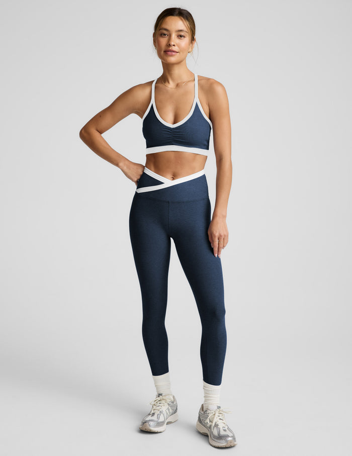 Woman wearing a navy sports bra and leggings with white accents on a light gray background.