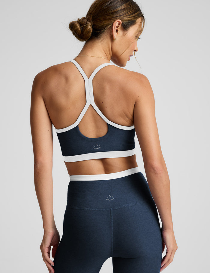 Woman wearing a navy sports bra and leggings with white accents on a light gray background.