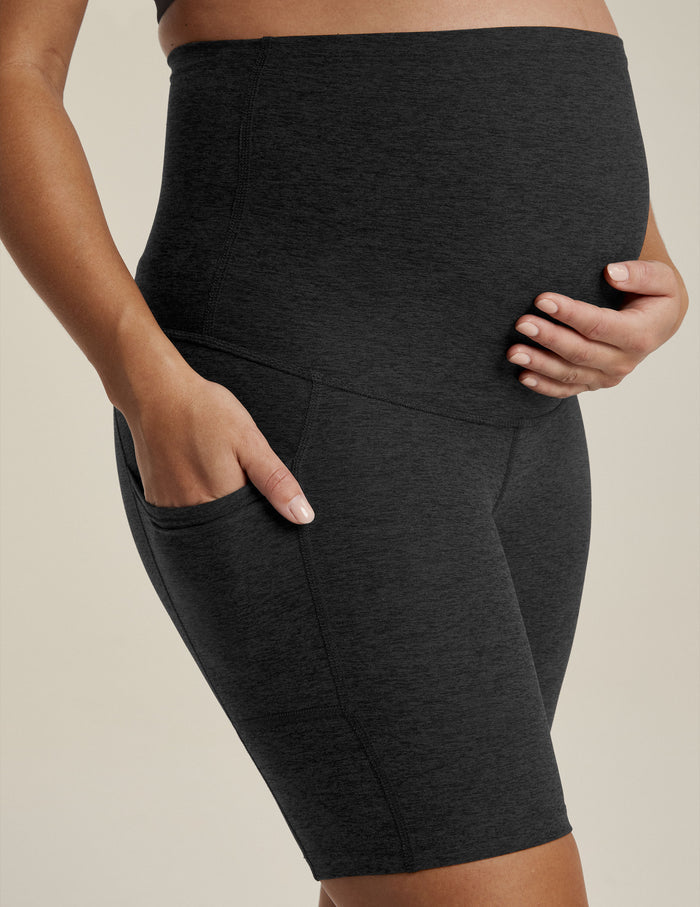Woman wearing Black marled Spacedye Pockets Forever Maternity Biker Short with hands on bump and in side pocket.