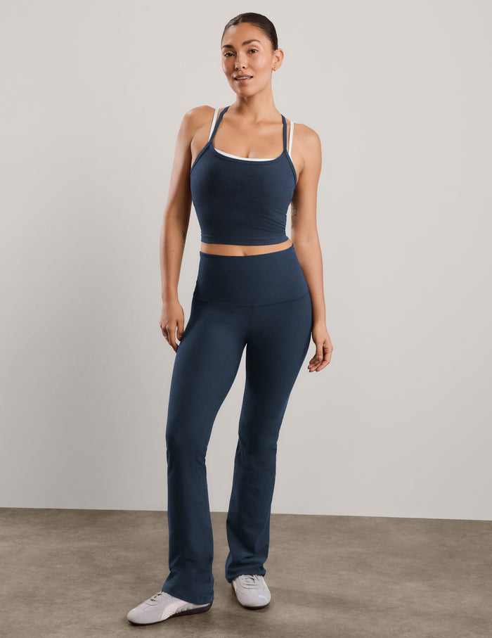 A woman modeling a matching athletic set consisting of a dark navy cropped tank with white trim and high-waisted dark navy blue bootcut pants, standing against a neutral studio backdrop.
