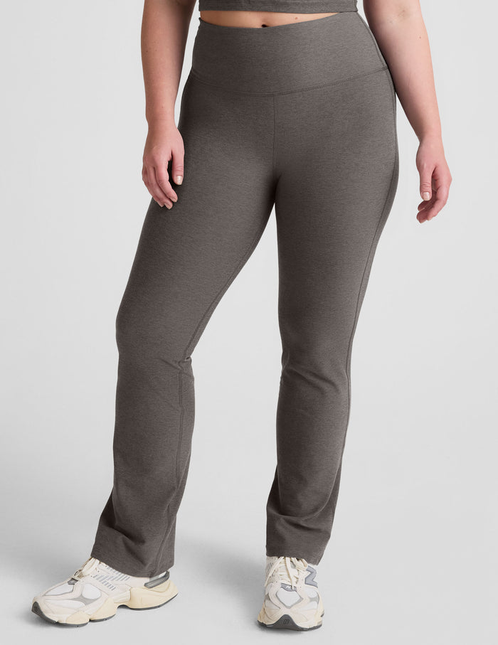 A woman wears dark gray Spacedye Practice High Waisted Bootcut Pants with a snug fit, wide waistband, and flared leg.