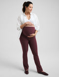 A pregnant woman wearing a white nursing bra, white button-up shirt, and red bootcut maternity leggings against a plain studio background.