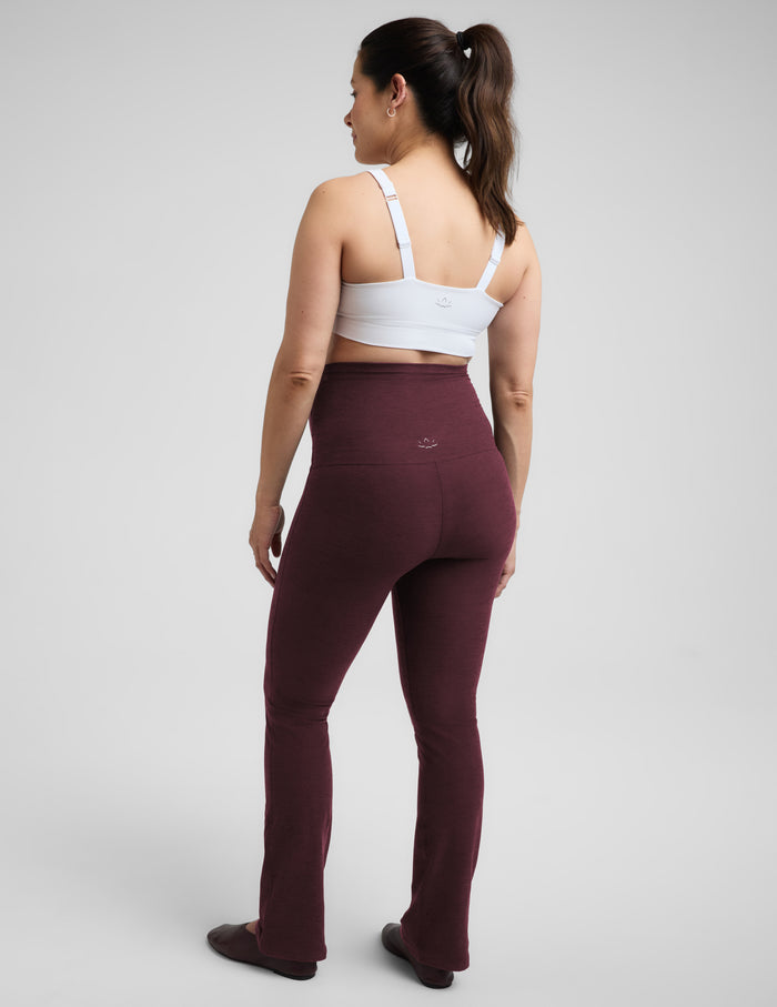 A pregnant woman wearing a white nursing bra and red bootcut maternity leggings against a plain studio background.