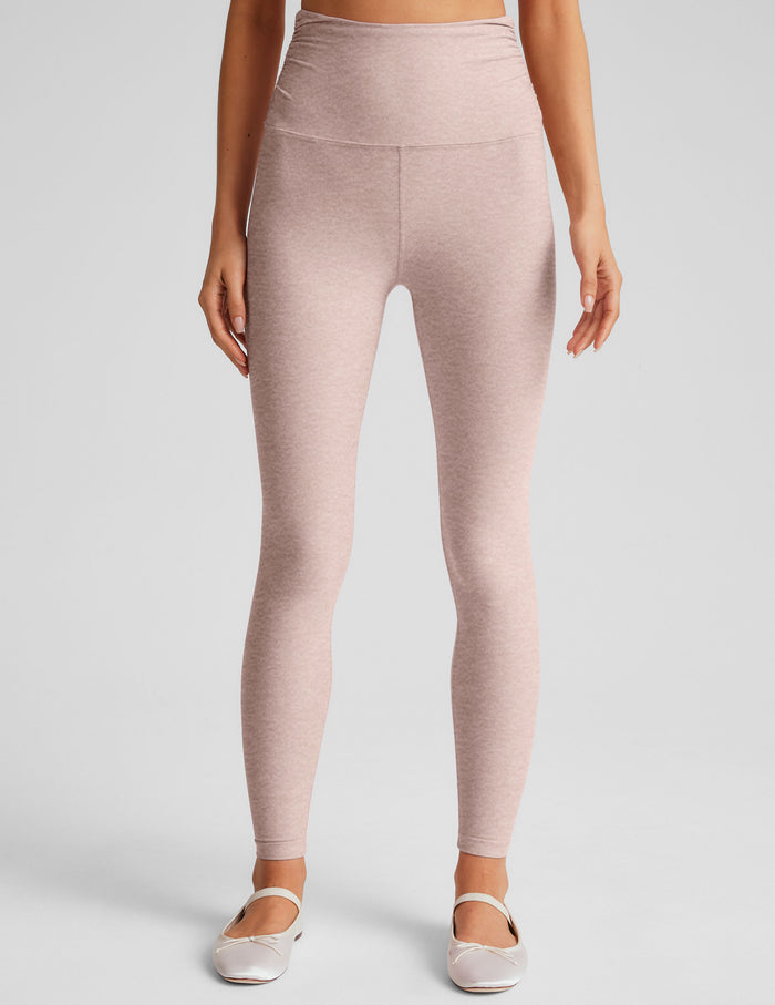 model wearing a pink cropped tank top and pink high-waisted midi length leggings on a plain background.