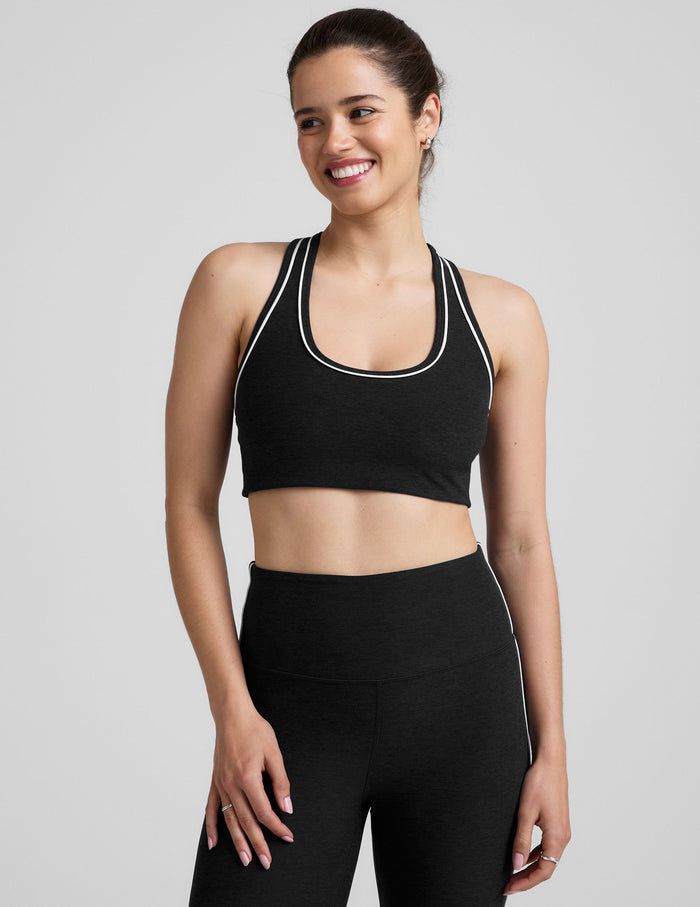 model wearing a black scoop neck racerback sports bra and leggings with white trim on a gray background.