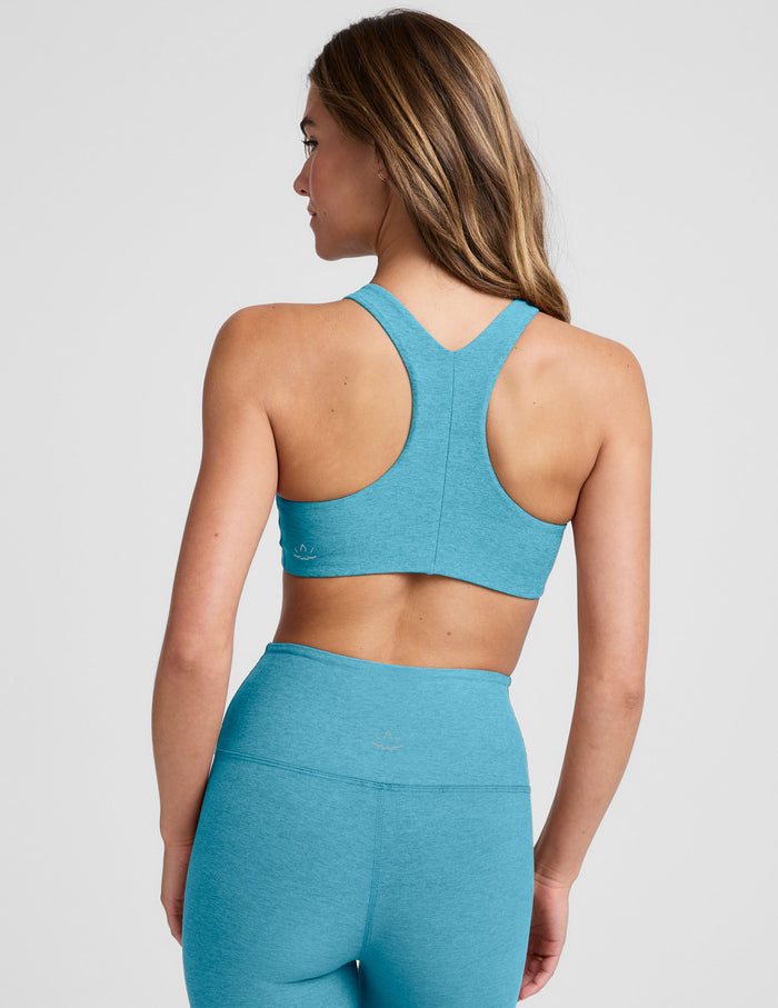 Woman wearing a blue high scoop neck racerback bra and leggings on a plain background.
