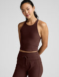 Woman wearing a brown high-neck racerback cropped tank and joggers against a plain background.