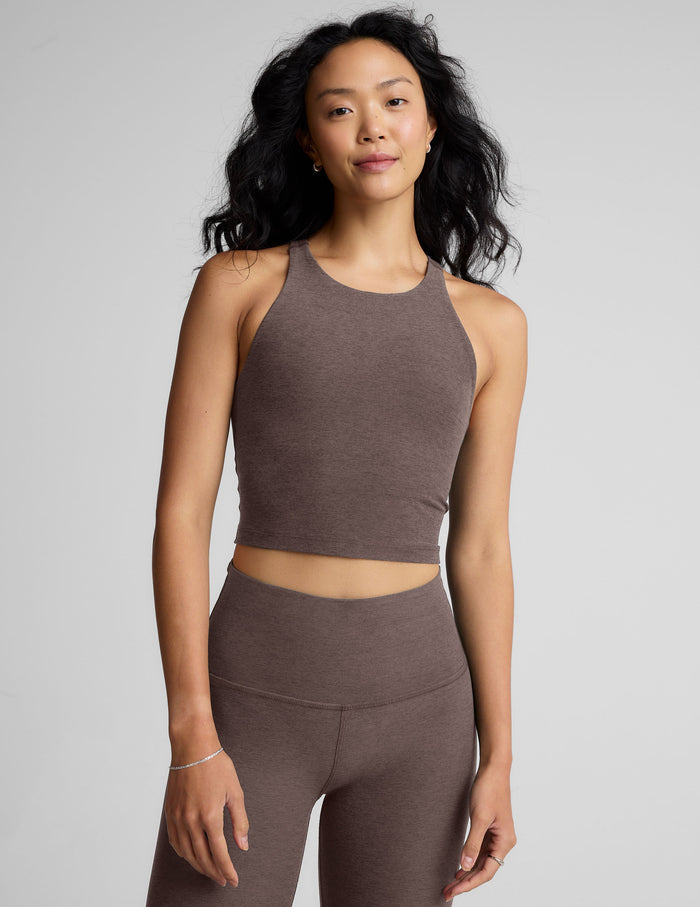 Woman wearing a brown high-neck racerback cropped tank and leggings against a gray background.