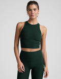 woman wearing a green high-neck racerback cropped tank and leggings on a plain background.