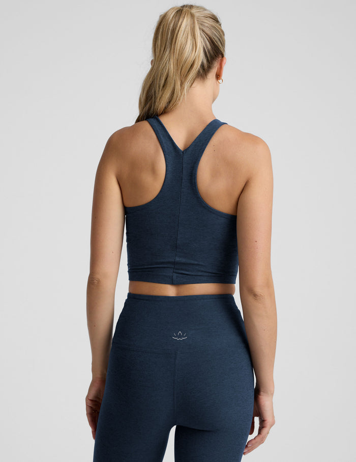 woman wearing a navy blue high neck cropped tank and leggings on a plain background.