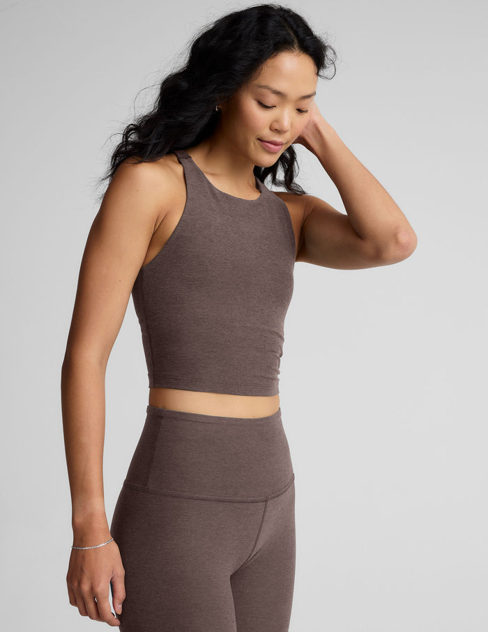 Woman wearing a brown high-neck racerback cropped tank and leggings against a gray background.