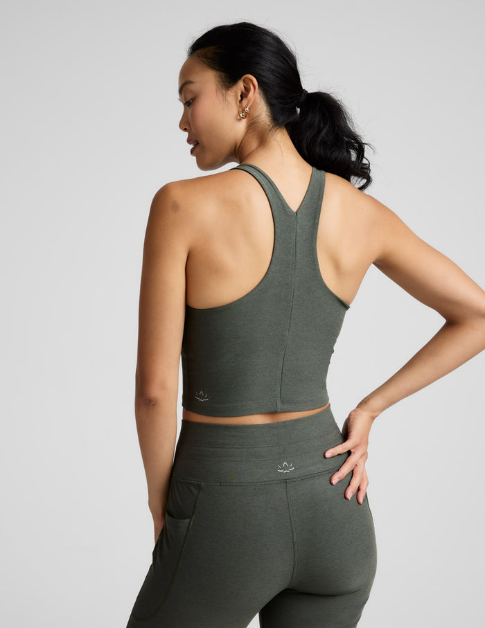 Woman is wearing a green racerback high-neck cropped tank and joggers against a plain background.