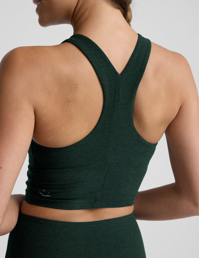 woman wearing a green high-neck racerback cropped tank and leggings on a plain background.