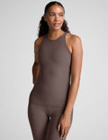 Woman wearing a brown high neck racerback tank top and leggings on a light gray background.