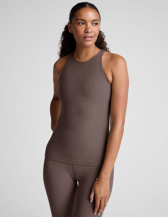 Woman wearing a brown high neck racerback tank top and leggings on a light gray background.