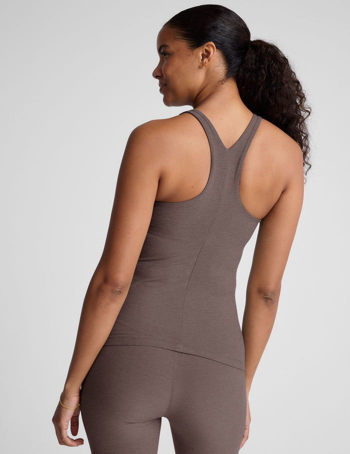 Woman wearing a brown high neck racerback tank top and leggings on a light gray background.