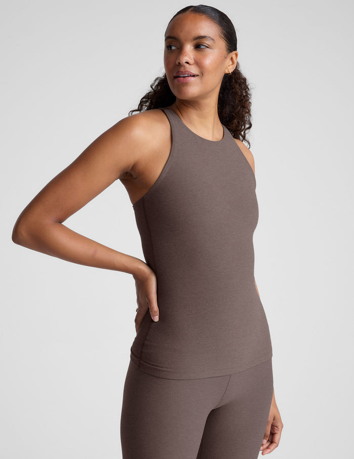 Woman wearing a brown high neck racerback tank top and leggings on a light gray background.
