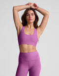 Woman wearing a purple sports bra and leggings against a plain background.